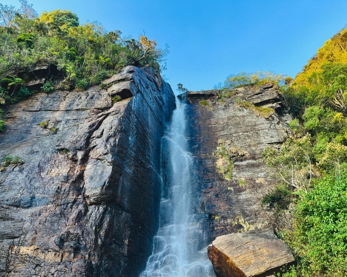 Lovers Leap Falls waterfall flowing down rock cliff with forest canopy and trees under blue sky Nuwara Eliya Sri Lanka