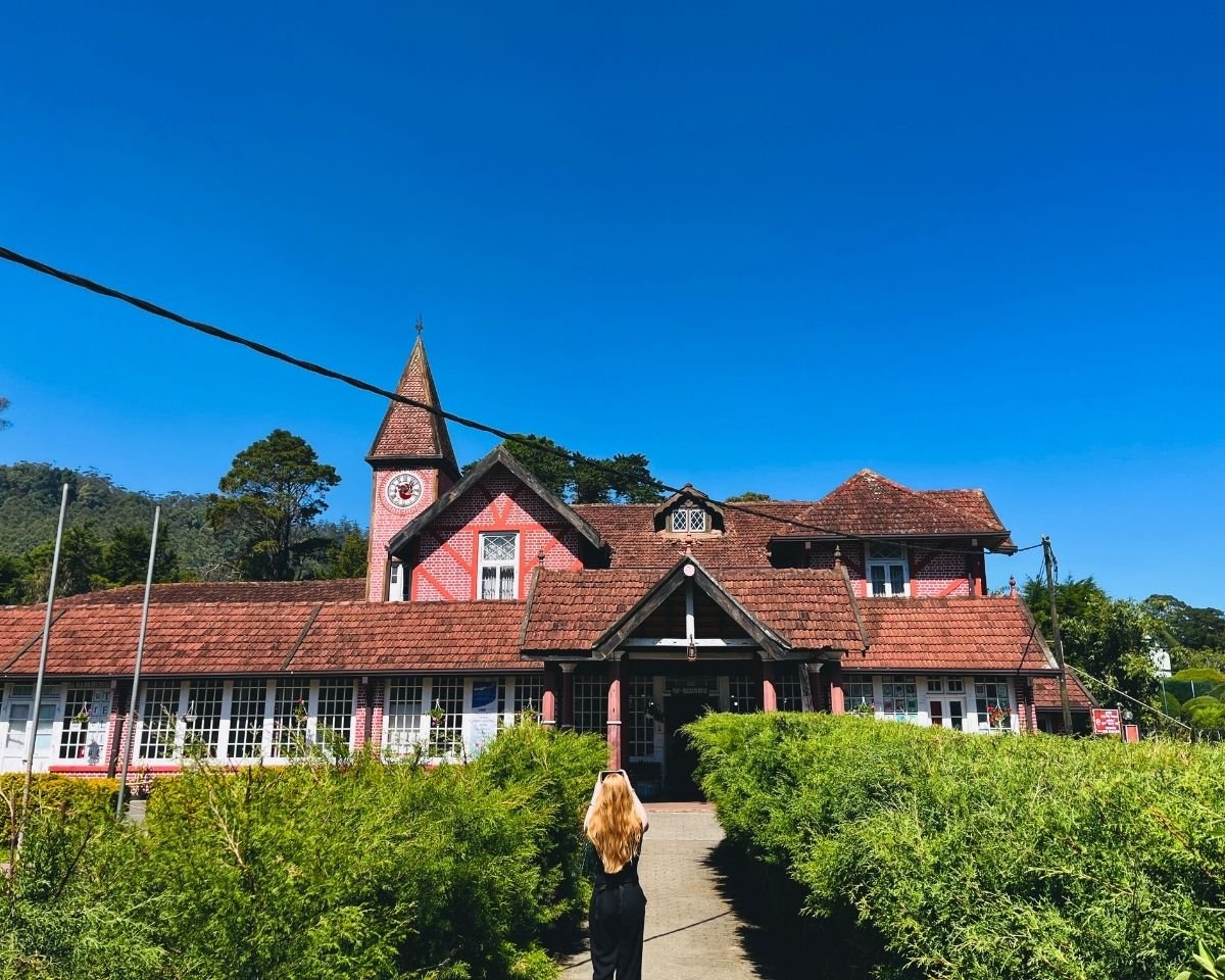 Tourist taking photo of Nuwara Eliya Post Office red brick Tudor building with clock tower under blue sky Sri Lanka