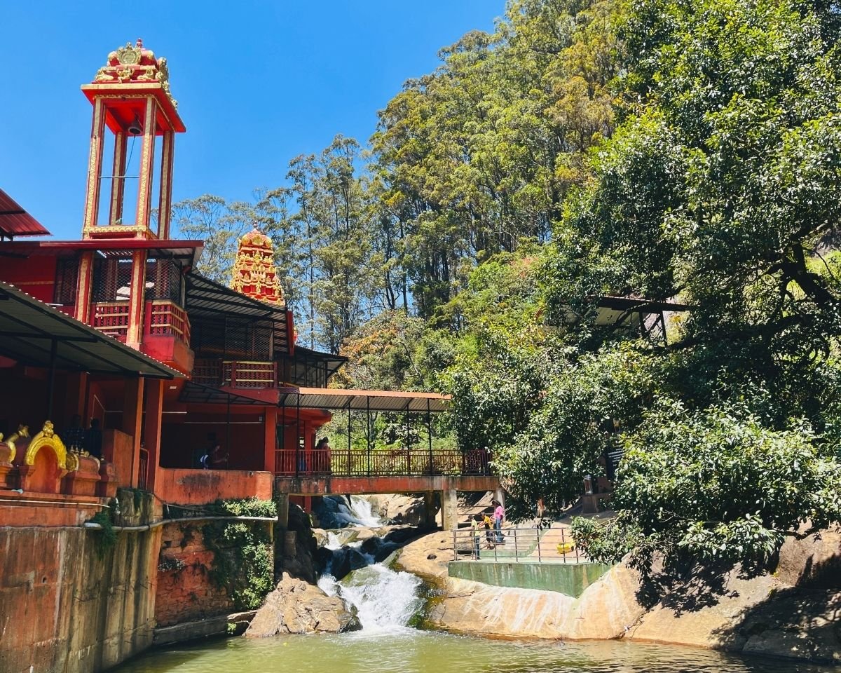 Seetha Eliya stream flowing beside red and gold bell tower at Seetha Amman Kovil Hindu temple in Nuwara Eliya, Sri Lanka with eucalyptus forest