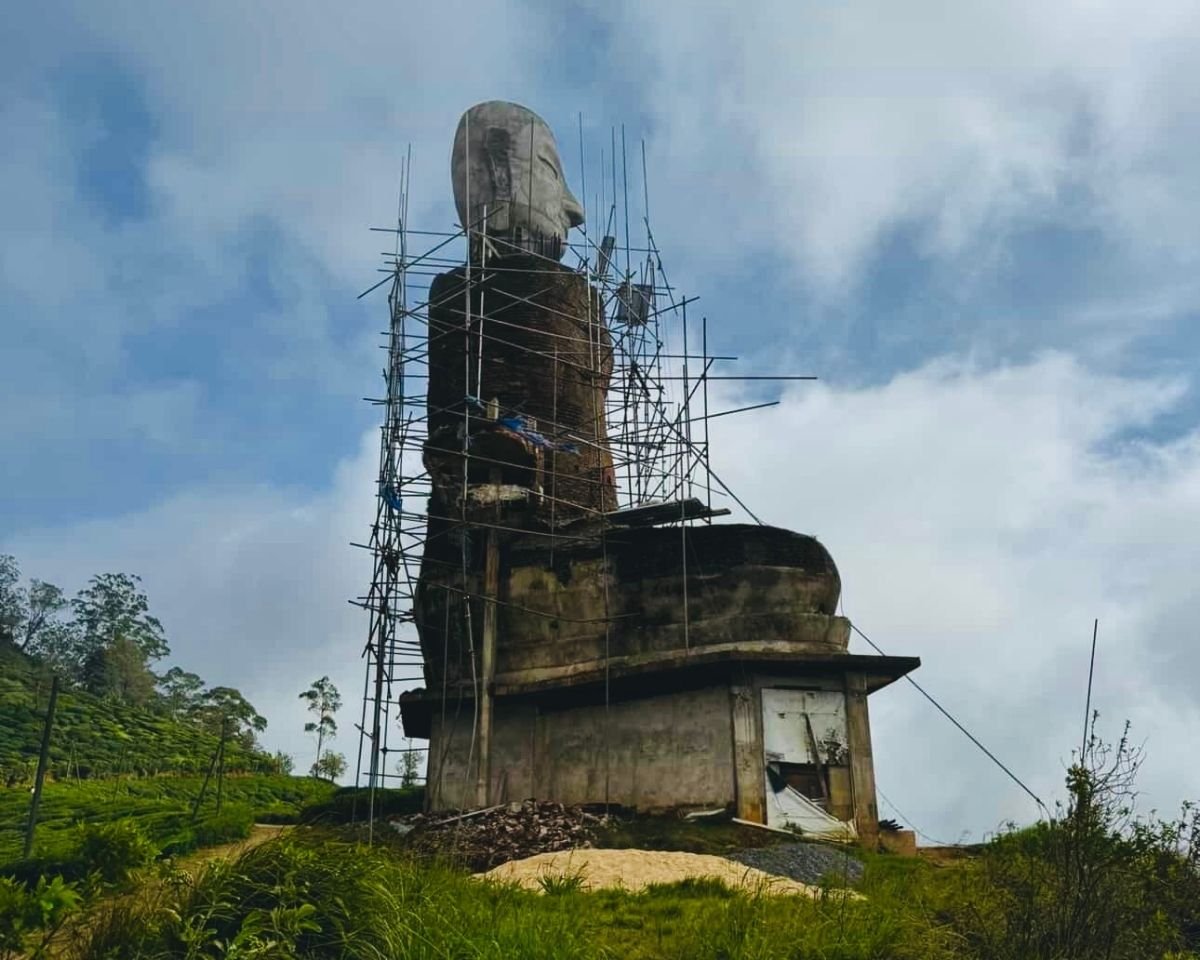 Unfinished Buddha statue under construction with scaffolding at Swarnagiri Maha Viharaya Single Tree Temple Nuwara Eliya Sri Lanka with blue sky and temple roof