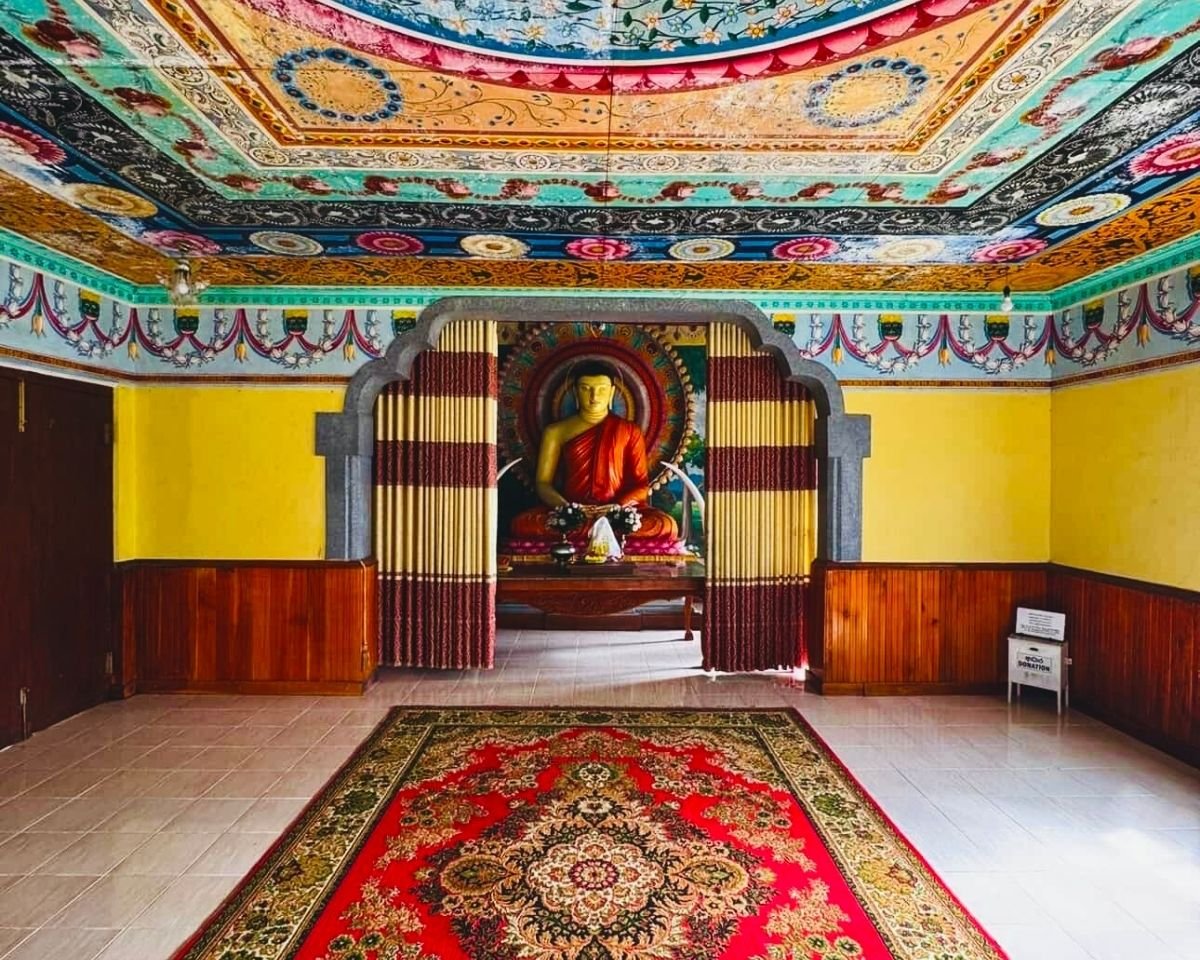Seated Buddha statue with colorful painted ceiling inside image house at Swarnagiri Maha Viharaya Single Tree Temple Nuwara Eliya