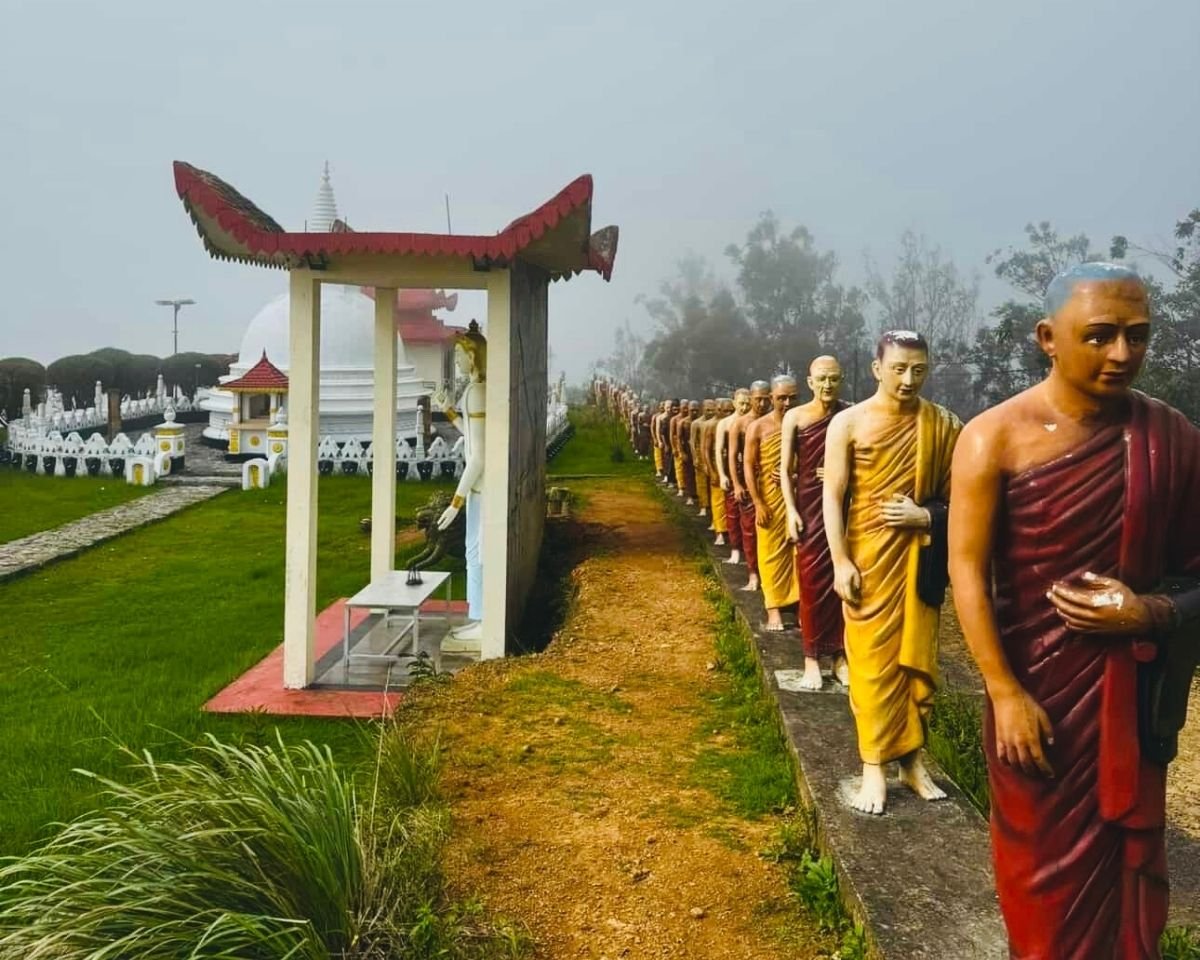 Line of monk statues in saffron and maroon robes with white stupa and misty hills at Swarnagiri Maha Viharaya Single Tree Temple Nuwara Eliya