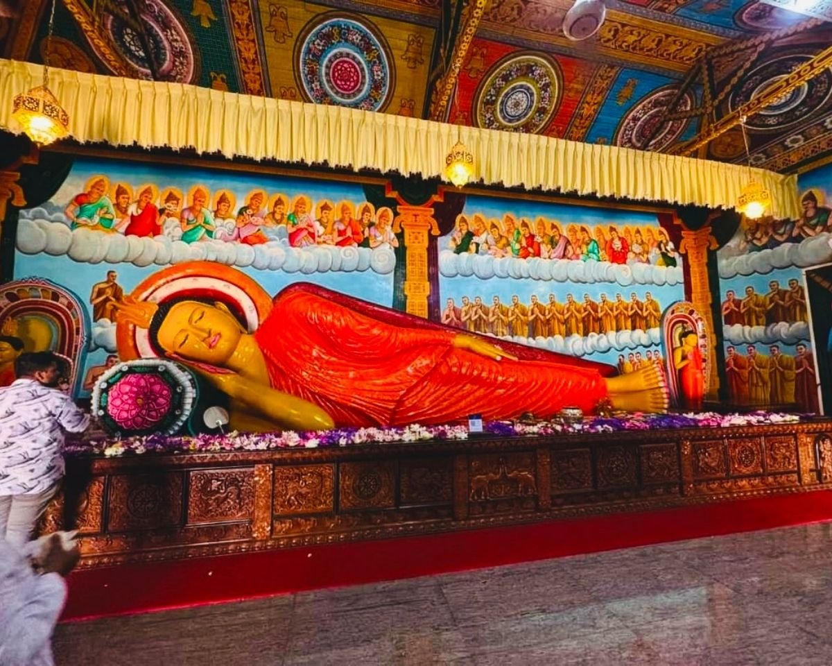 Reclining Buddha statue with colorful ceiling murals and devotees inside image house at Swarnagiri Maha Viharaya Single Tree Temple Nuwara Eliya