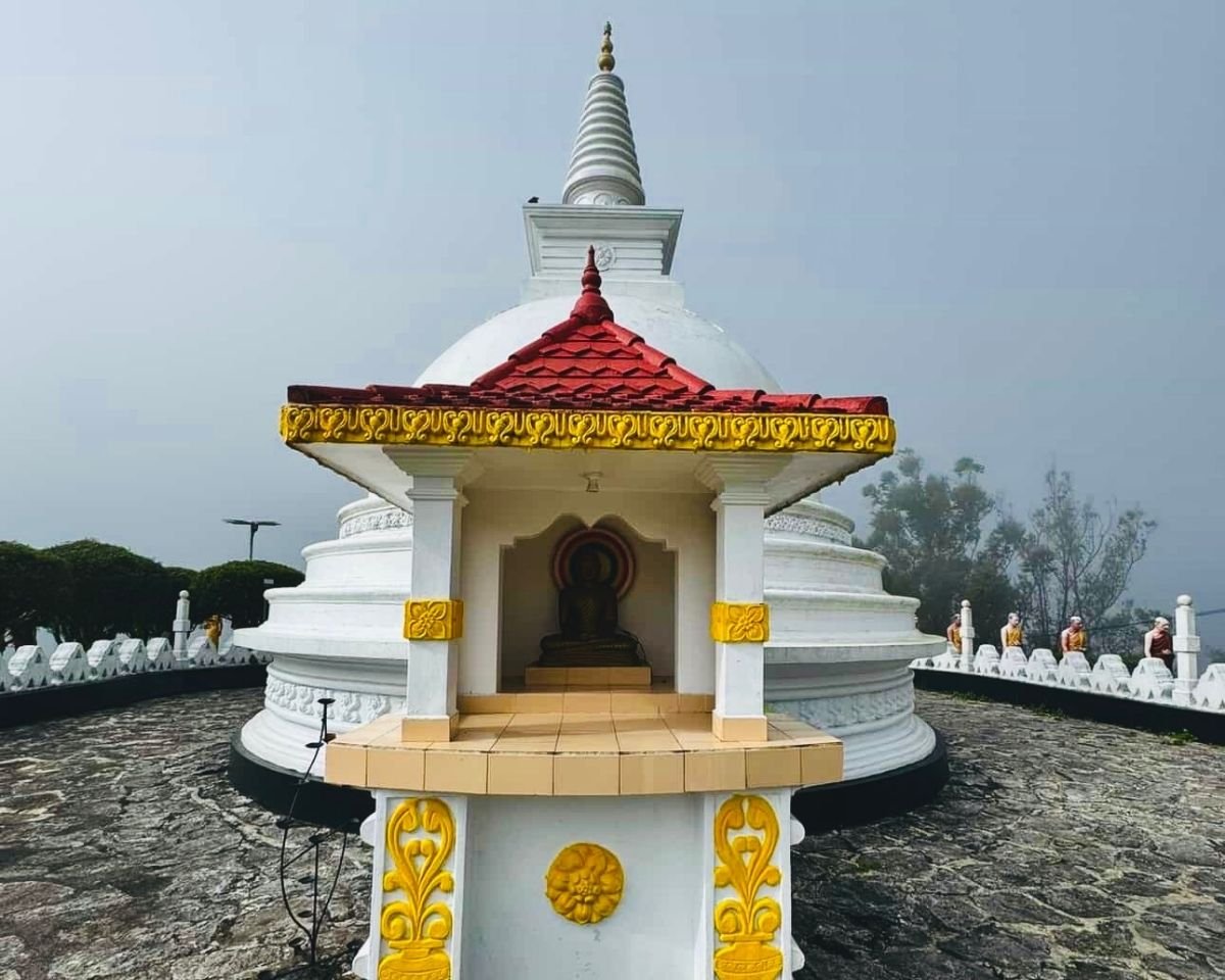 Buddha shrine with red roof and yellow lettering in front of white stupa at Swarnagiri Maha Viharaya Single Tree Temple Nuwara Eliya