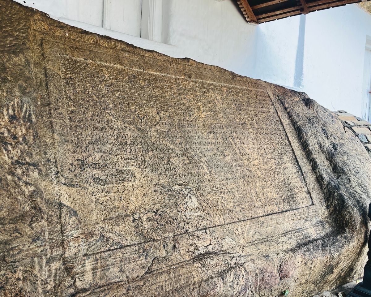 Large ancient Sinhala rock inscription carved into natural boulder surface under white temple building at Dambulla Royal Cave Temple complex Sri Lanka