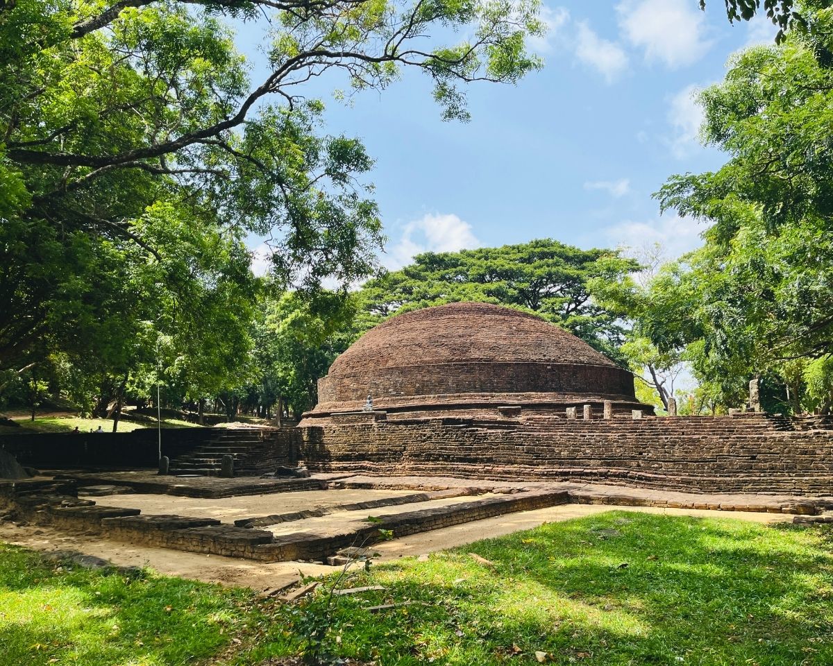 Ancient red brick dome stupa surrounded by green trees and grassy courtyard at Dambulla Somawathiya archaeological site Sri Lanka