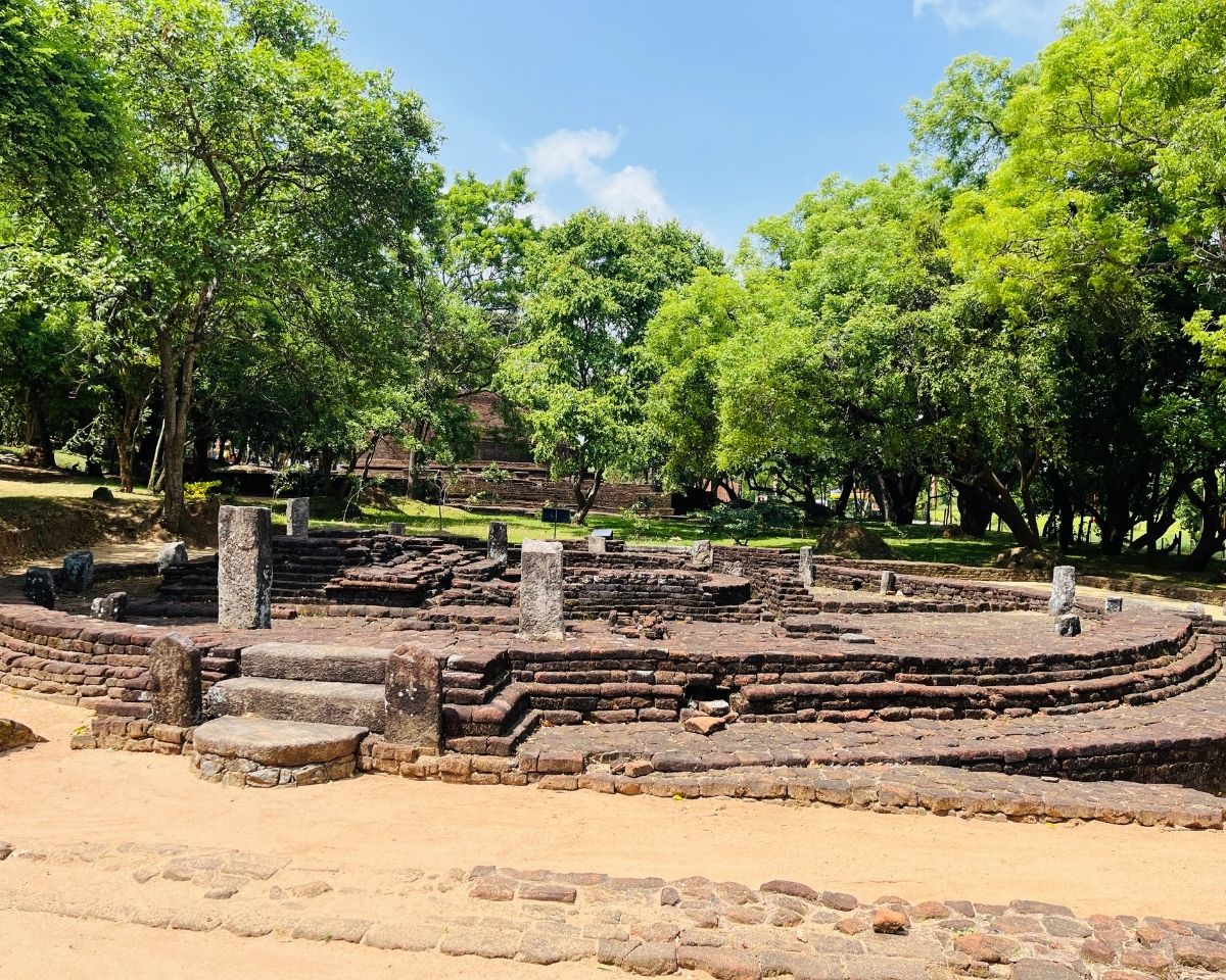Circular ancient brick ruins of Bodhighraya Bodhi Tree Shrine with stone pillars and steps surrounded by green trees at Dambulla Somawathiya archaeological site Sri Lanka