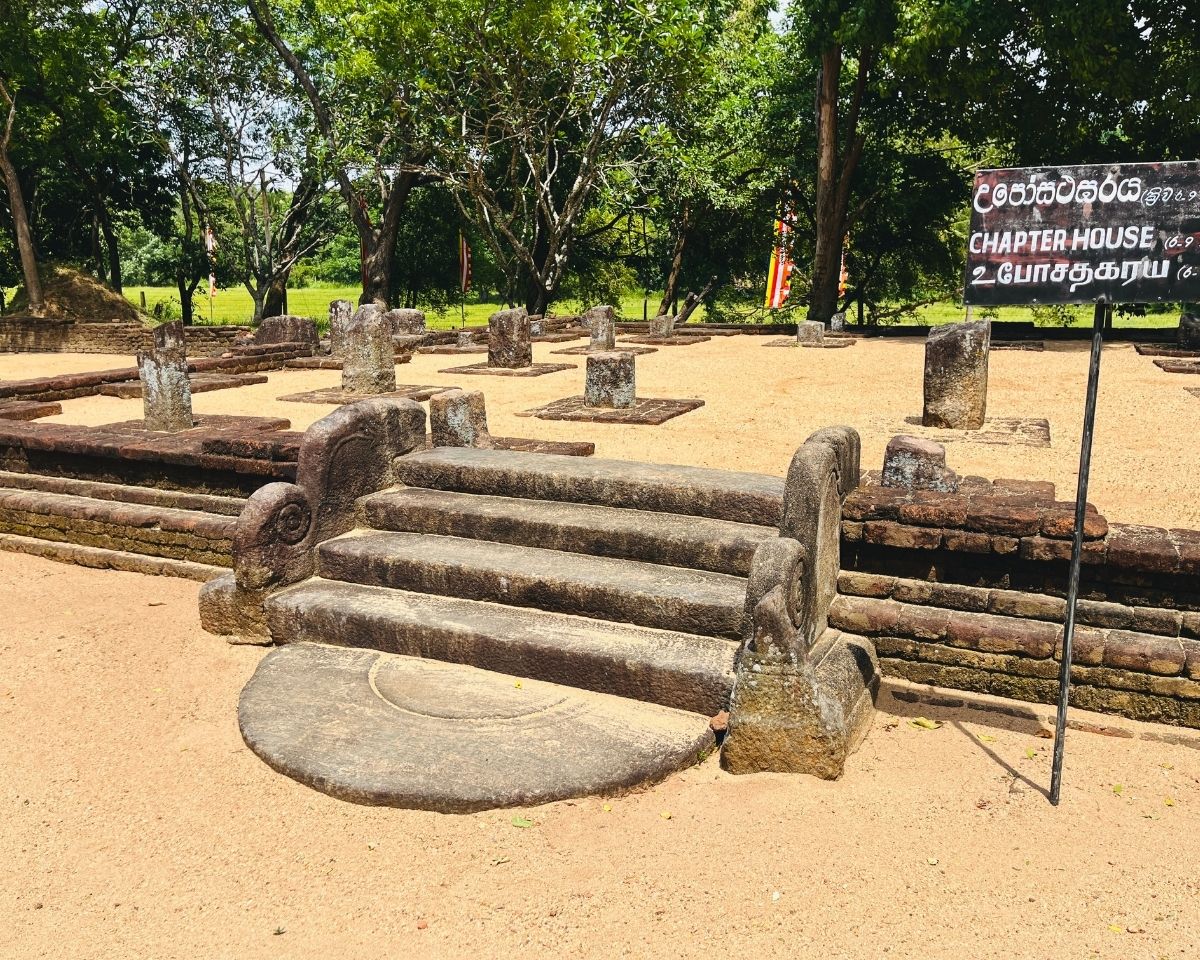 Ancient stone steps with carved balustrades leading to Chapter House Uposathagaraya ruins with stone pillars on sandy ground and black signboard at Dambulla Somawathiya Sri Lanka