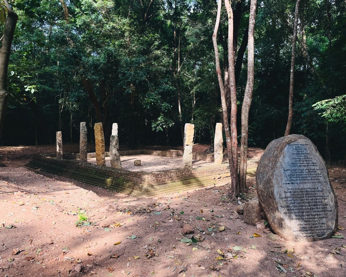 Ancient temple ruins foundation with standing stone pillars and large inscribed stone monument in Jathika Namal Uyana ironwood forest Dambulla Sri Lanka