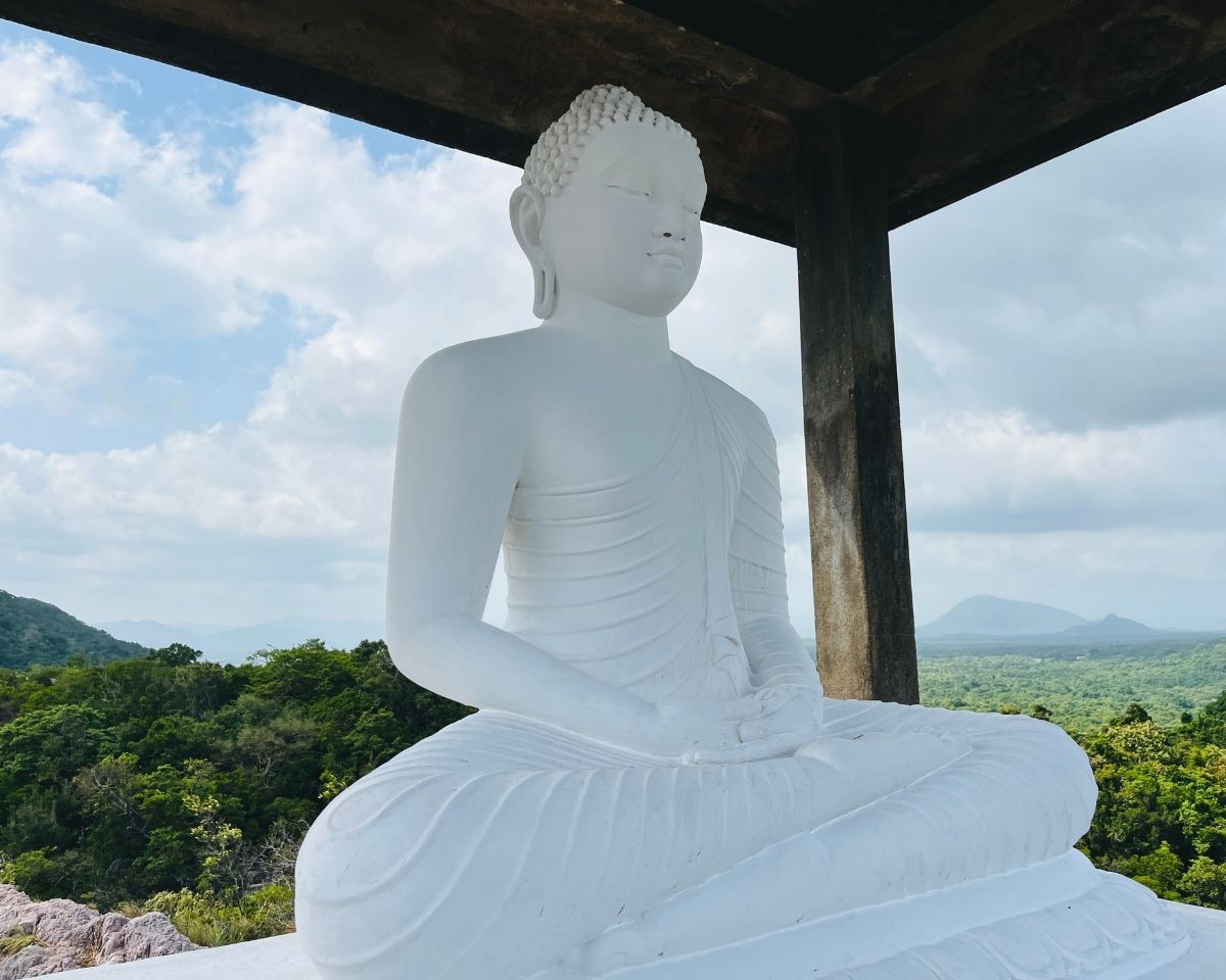 White Buddha statue in meditation pose close up at summit shrine on Pink Quartz Mountain overlooking green ironwood forest in Jathika Namal Uyana Dambulla Sri Lanka