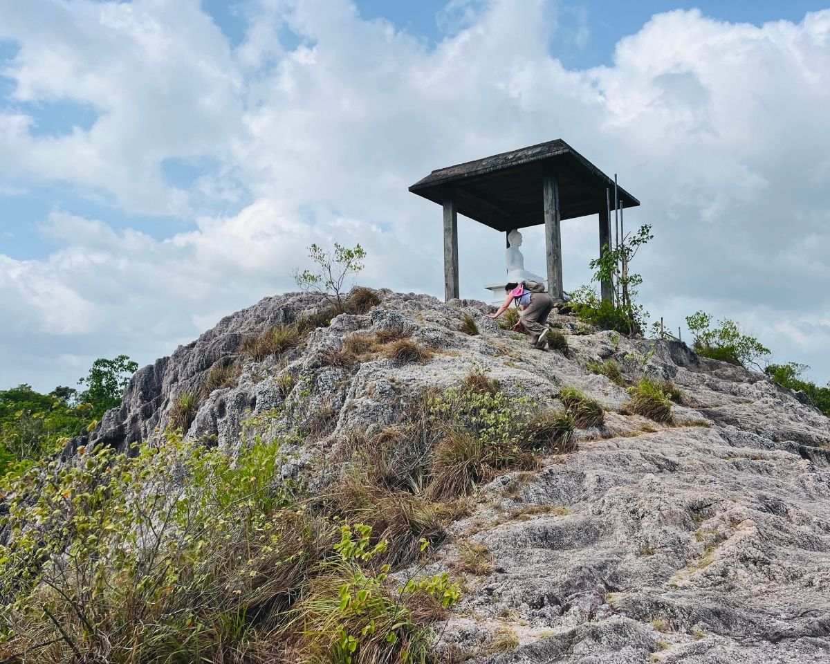 White Buddha statue shrine on rocky summit of Pink Quartz Mountain with hiker climbing grey quartz rocks in Jathika Namal Uyana Dambulla Sri Lanka