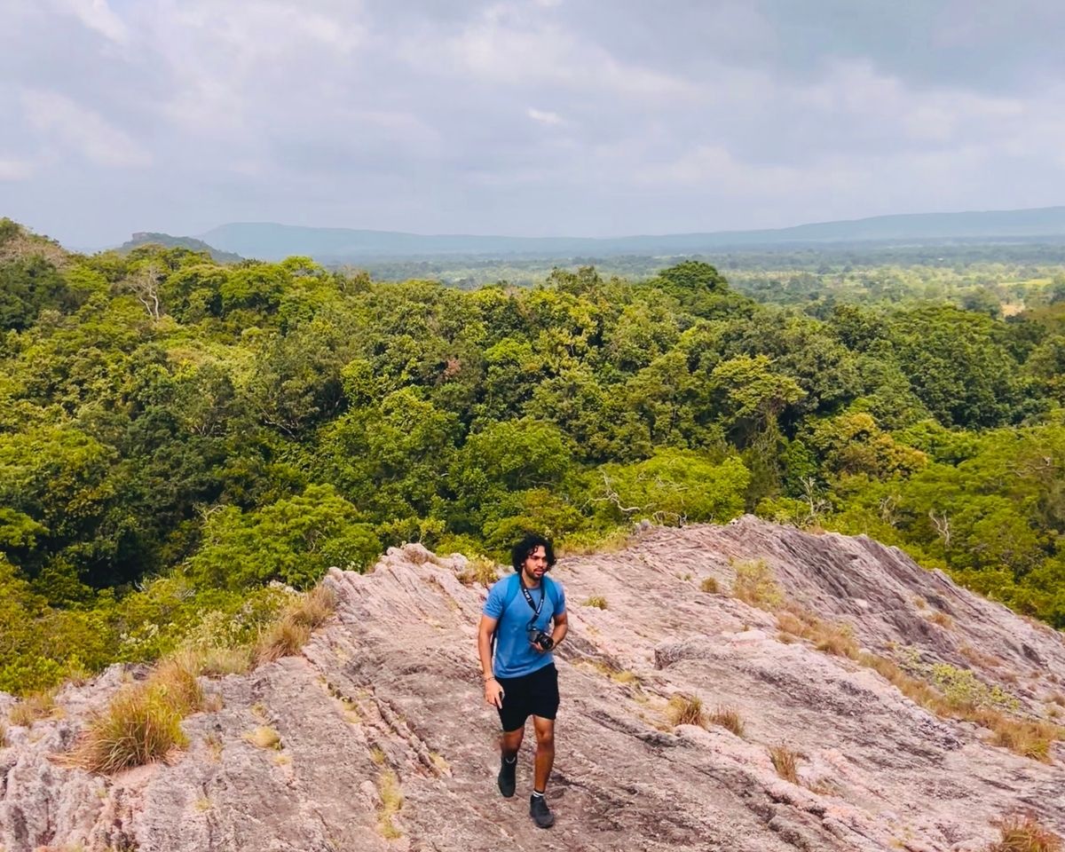 Man hiking on pink quartz rock ridge at the top of Pink Quartz Mountain with panoramic ironwood forest view in Jathika Namal Uyana Dambulla Sri Lanka